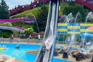 Guest splashing down a steep water slide at Water Wizz water park in East Wareham, Massachusetts, surrounded by fountains and family attractions.