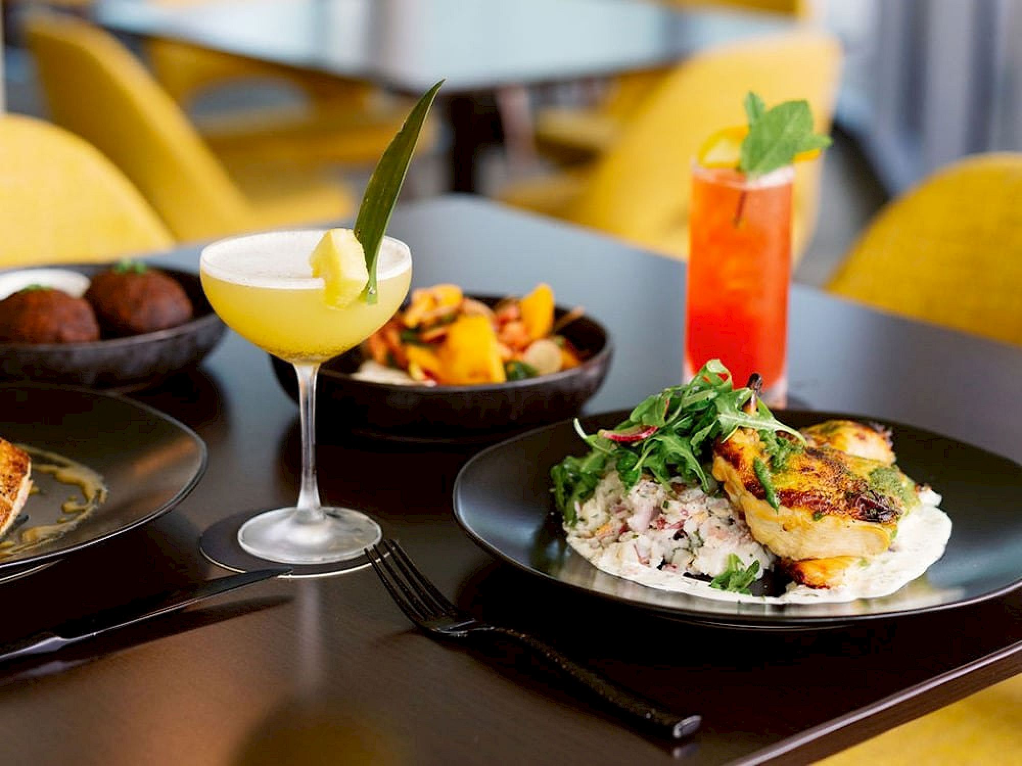 A beautifully plated gourmet meal with fresh salad, vibrant cocktails, and appetizers served at the signature restaurant inside Hotel ELEO at the University of Florida.