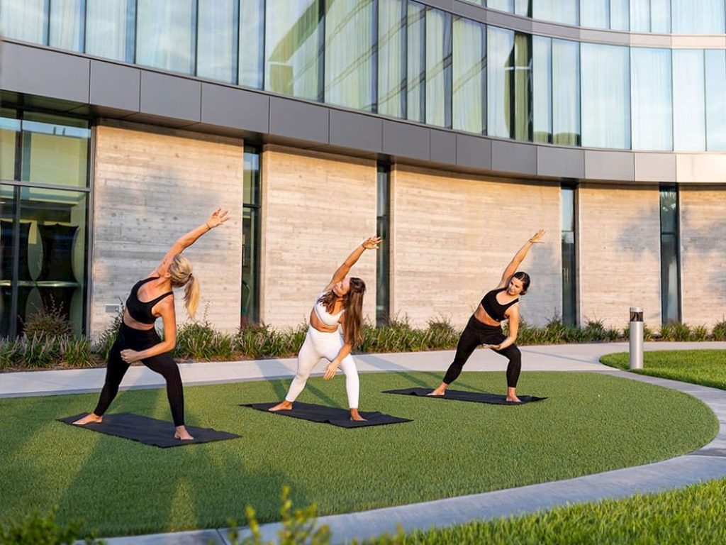 Guests participating in an outdoor yoga session on the terrace at Hotel ELEO at the University of Florida, surrounded by modern architecture and lush green space.
