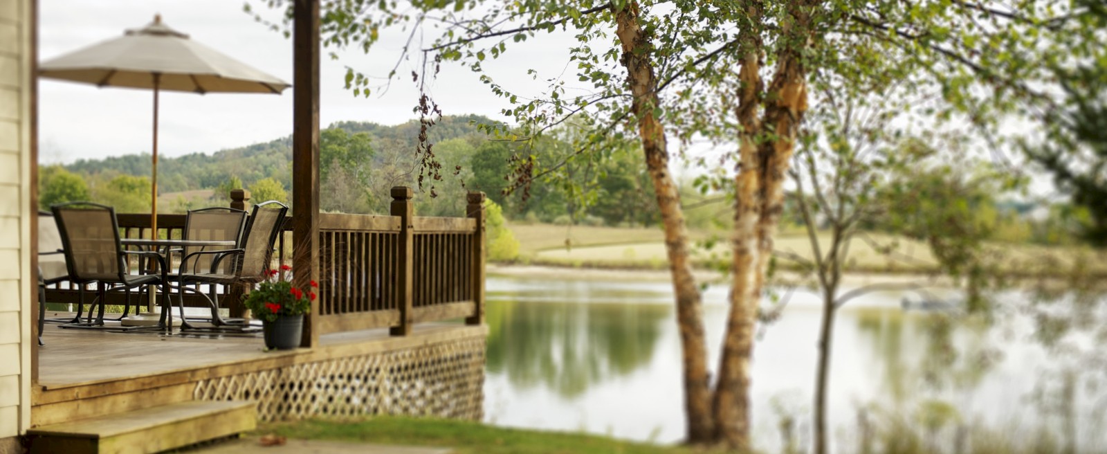 Peaceful lakeside cabin deck with patio furniture and umbrella at Stonewall Resort in Roanoke, West Virginia, overlooking calm water and scenic hills.