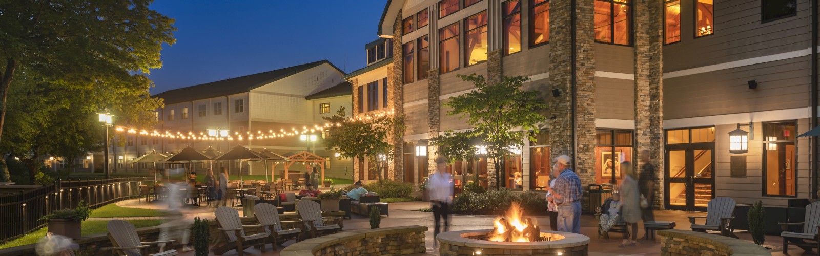 Evening view of the Stonewall Resort outdoor patio with fire pit, string lights, and guests relaxing under a clear night sky in Roanoke, West Virginia.