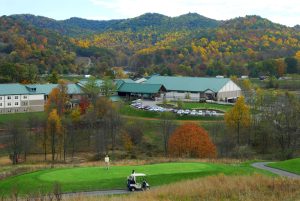 A scenic view of Stonewall Resort in Roanoke, West Virginia, surrounded by colorful autumn hills with guests golfing on the lush green course.