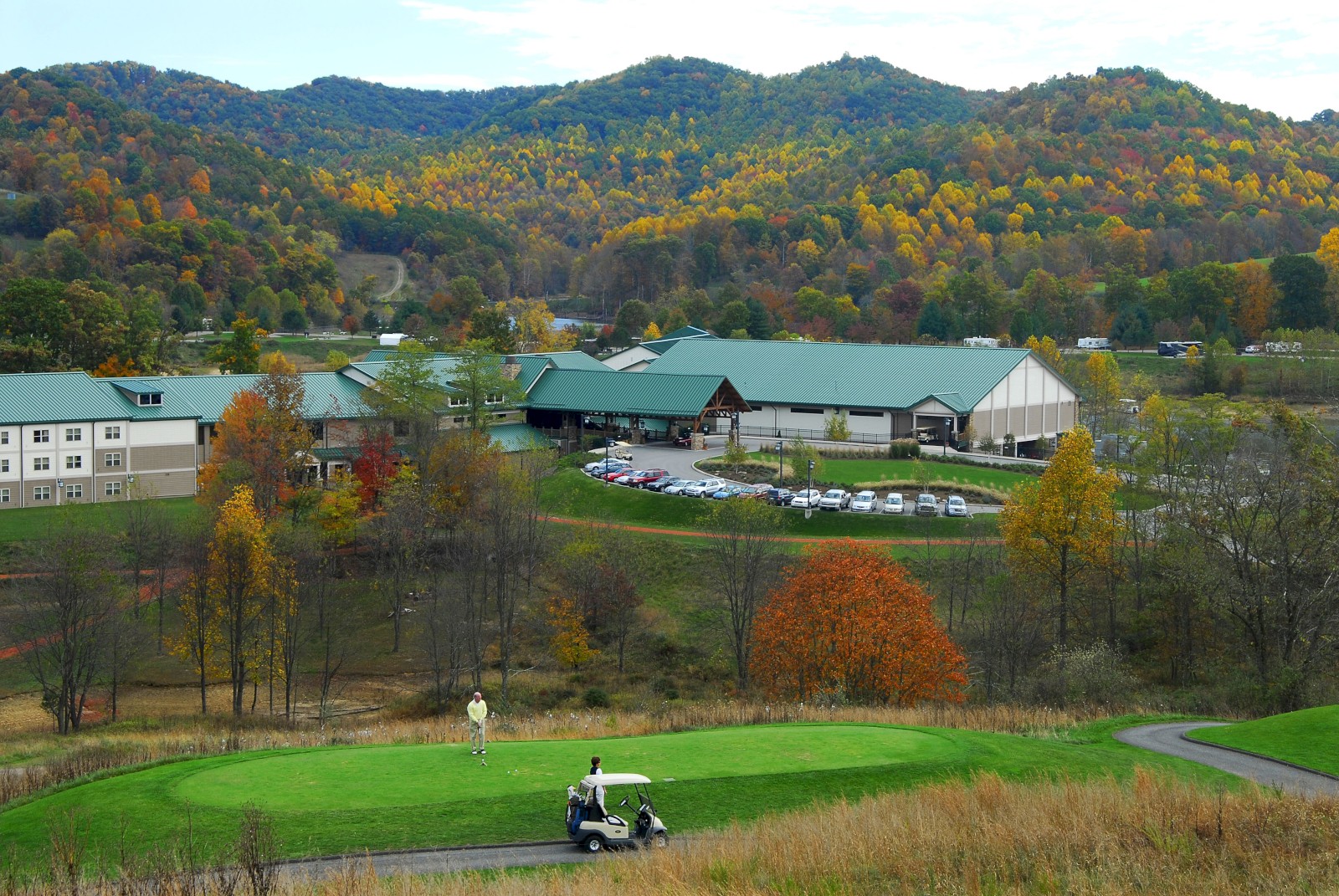 A scenic view of Stonewall Resort in Roanoke, West Virginia, surrounded by colorful autumn hills with guests golfing on the lush green course.