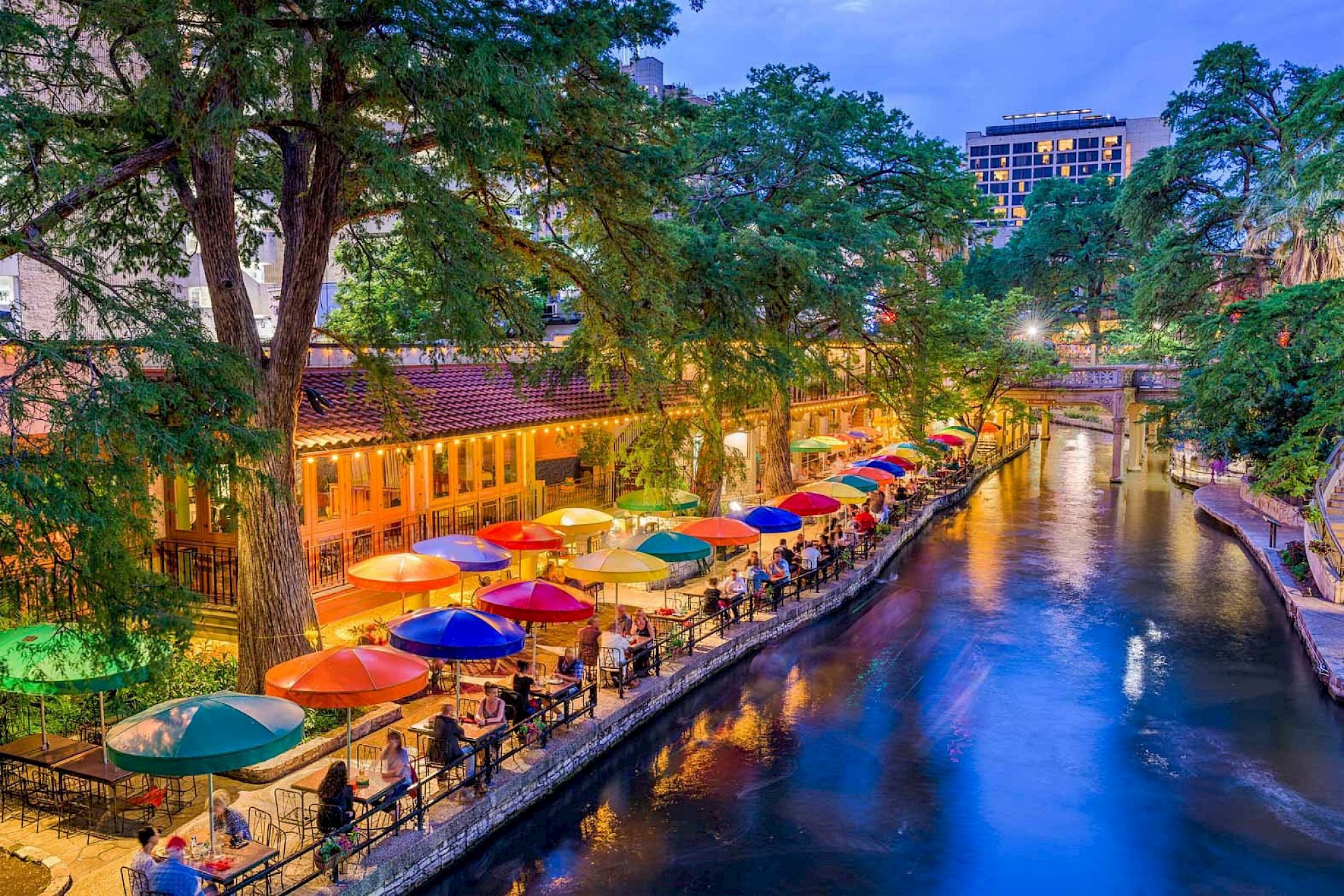 San Antonio River Walk scene near Crockett Hotel with restaurants and colorful umbrellas.